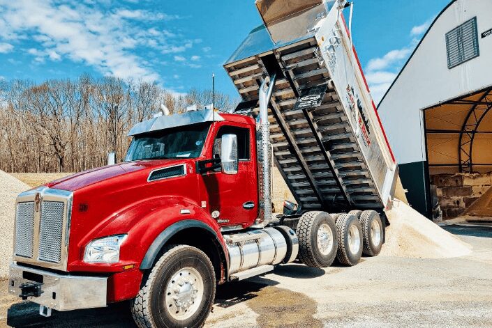A red Eastside Bulk dump truck tipping outside a warehouse