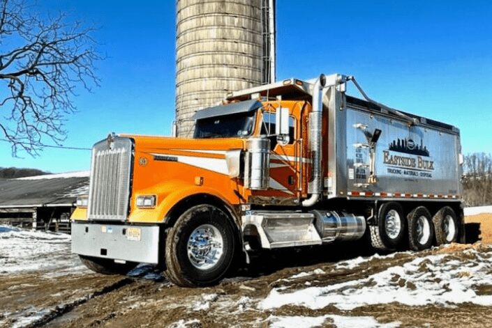 An orange Eastside Bulk dump truck beside a silo