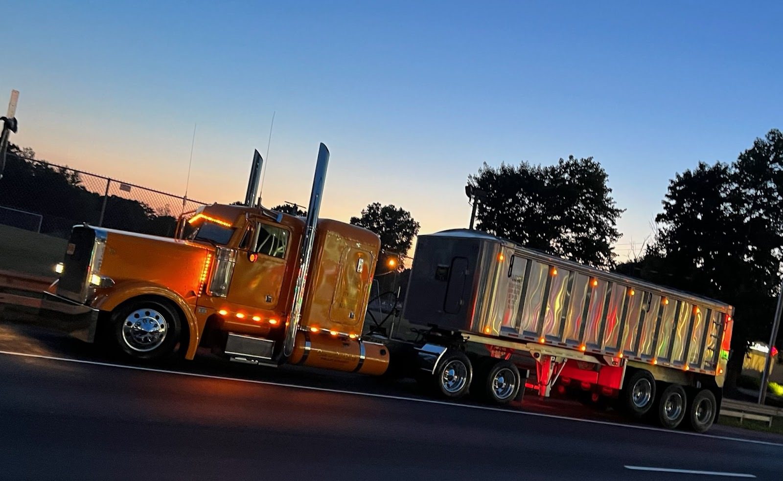 A gold Eastside Bulk Peterbilt pulling an aluminium dump trailer at dusk
